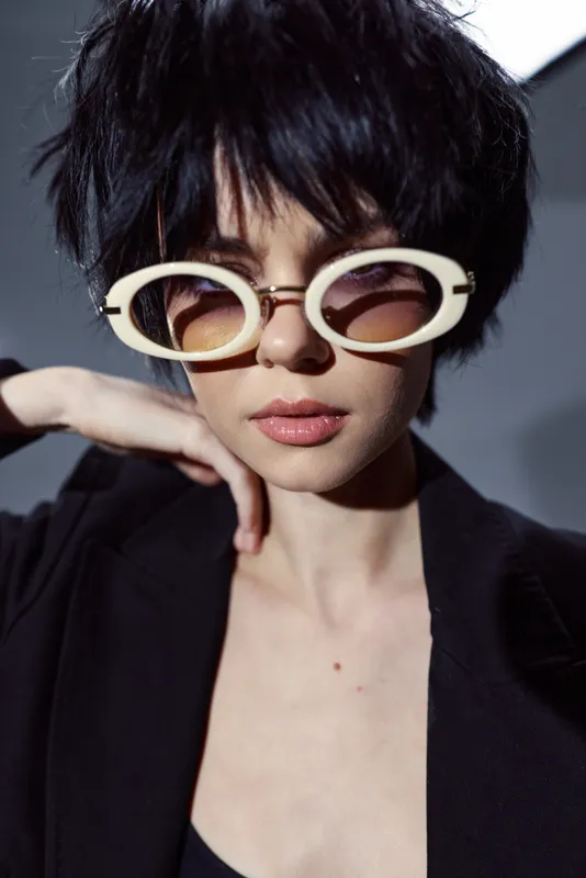 Stylish woman with short dark hair wearing retro white sunglasses and black outfit with confident expression and modern fashion style.