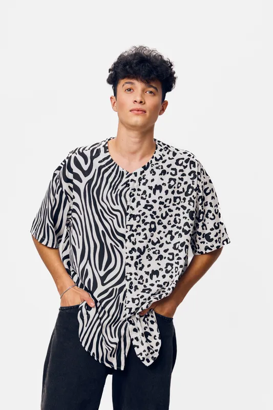 Young man wearing animal print shirt with zebra and leopard patterns confidently posing with hands in pockets against plain white background, casual fashion style.