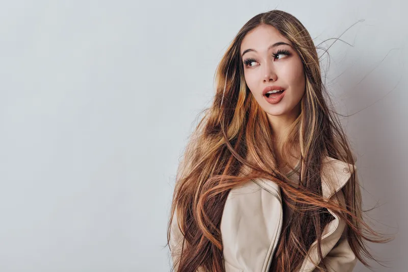 Young woman with long hair wearing beige coat looking sideways studio portrait isolated on grey background. Female beauty model with natural makeup and expression for fashion or lifestyle.