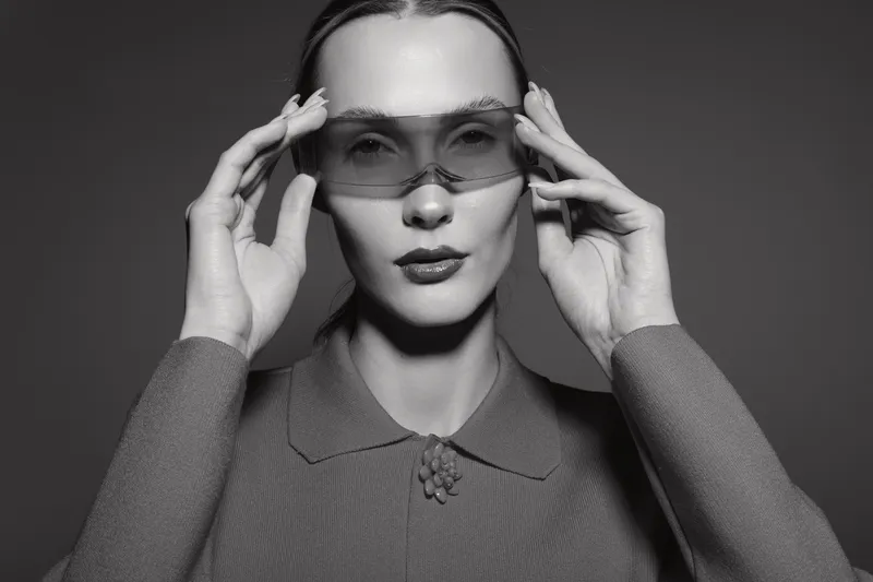 Portrait of a young Caucasian woman with fair skin wearing transparent sunglasses and a textured sweater in monochrome studio lighting. Fashion and style concept.