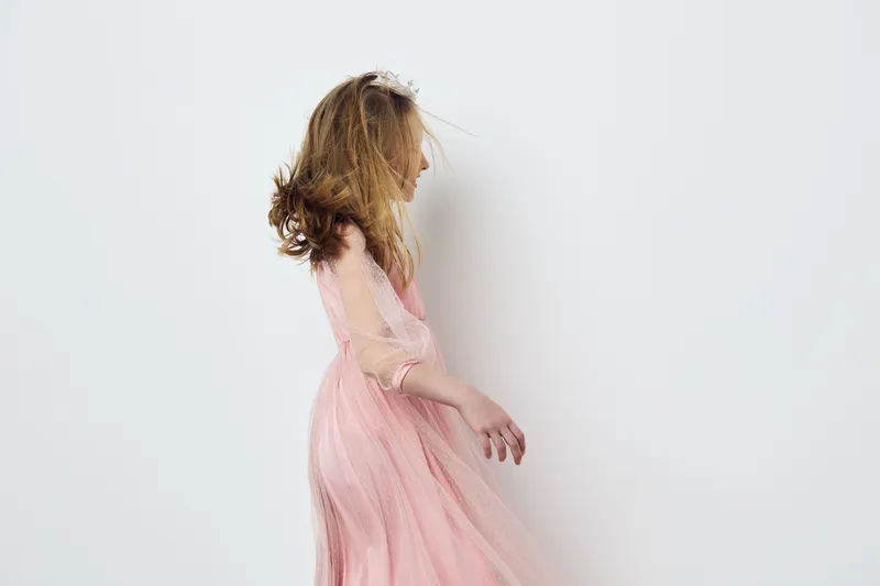 Graceful girl in a flowing pink dress, smiling joyfully against a soft pastel background Capturing innocence, beauty, and childhood wonder