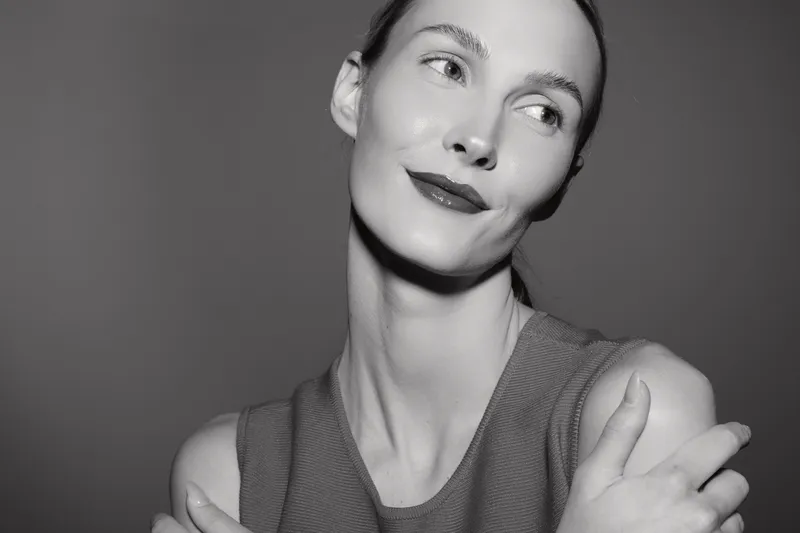 Portrait of a fair skinned white woman with dark hair in a sleeveless top smiling softly in studio. Concept of beauty, confidence, and natural elegance.