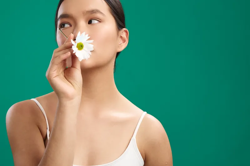 asian woman holds a white flower near her face against a solid green background, a calm, serene portrait that emphasizes natural beauty and minimalist mood.