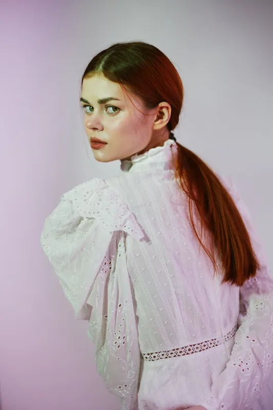 Young model in white vintage dress, showcasing emotional expression and soft lighting against a pastel background, highlighting modern fashion aesthetics in a seasonal context