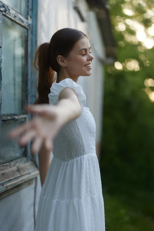 Young woman in a white dress reaching out joyfully, surrounded by nature, showcasing serenity and happiness, perfect for seasonal or lifestyle themes