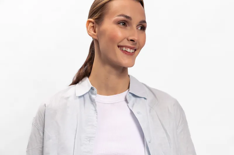 Smiling woman with light brown hair wearing white shirt and light jacket looks to side against white background. Natural expression and casual outfit create relaxed and positive mood.