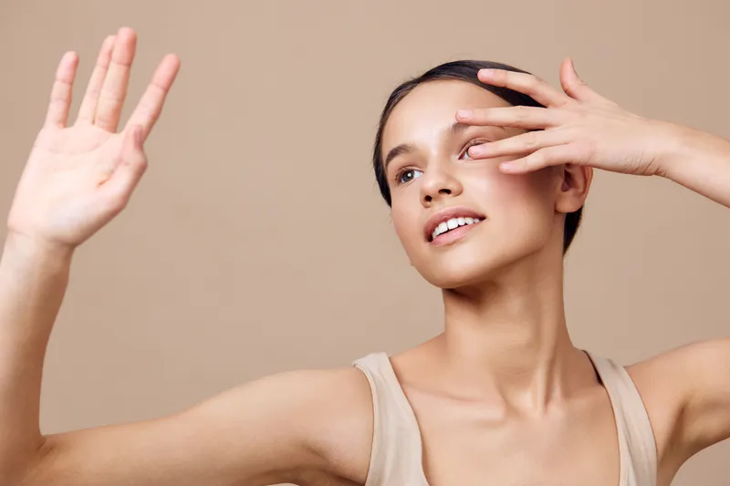 Young woman with natural beauty, wearing a beige top, showcasing confidence and joy against a warm, neutral background, perfect for beauty and skincare concepts