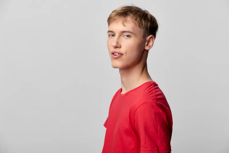 Young male model in a red t shirt against gray backdrop, showcasing casual fashion, confident pose, and lifestyle for marketing visuals and apparel campaigns.