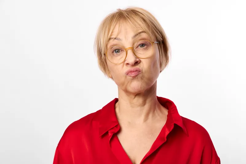 Woman with glasses portrait in studio, red shirt, short blonde hair, neutral concerned expression, looking at camera, closeup headshot against white background, even light
