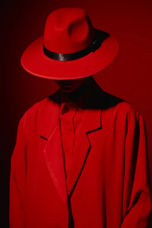 Creative fashion portrait of a person wearing a red fedora hat and matching vibrant jacket in dramatic lighting, emphasizing bold color contrast and mysterious style.
