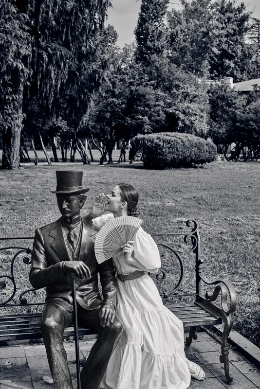 Vintage couple on a park bench, woman in a flowing dress holding a fan, man in a top hat, romantic scene in a timeless atmosphere