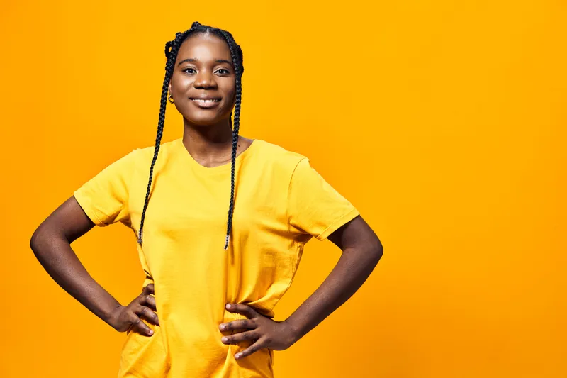 Confident young Black woman in a bright yellow t shirt posing cheerfully against a vibrant yellow background, showcasing positivity and self assurance