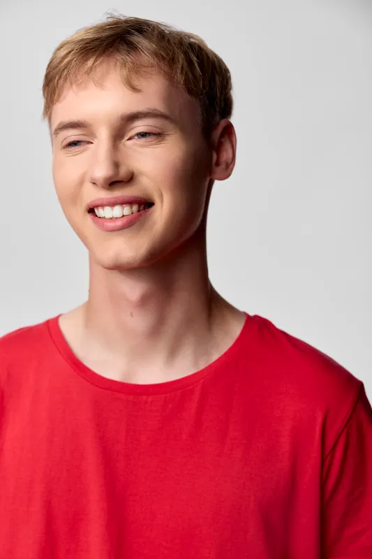 Smiling young man in a red casual shirt enjoying a light moment, relaxed posture and warm expression for lifestyle, happiness, and everyday charm in modern fashion photography.