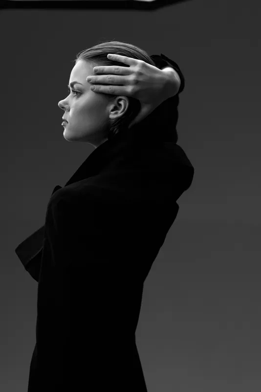 Black and white portrait of a thoughtful woman in a dark coat with braided hair in profile