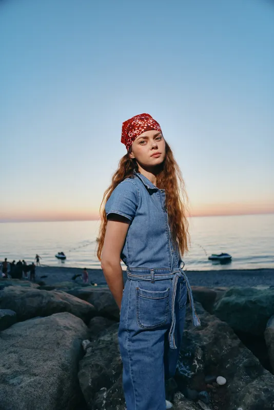 lifestyle woman in modern boho-western denim street style wearing red bandana by the seaside during golden hour with natural lighting, film color effect