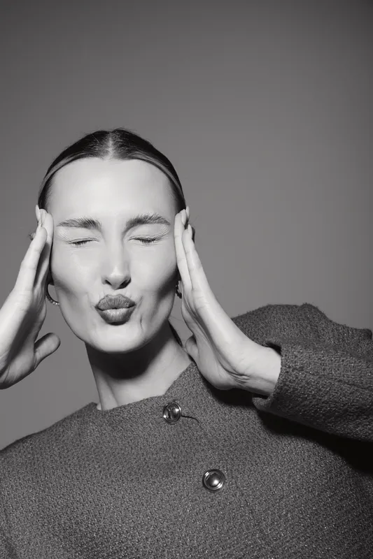 Young white woman with light skin and closed eyes makes playful kiss face with hands near head. Studio portrait in black and white. Concept for fun, expression, and emotion.