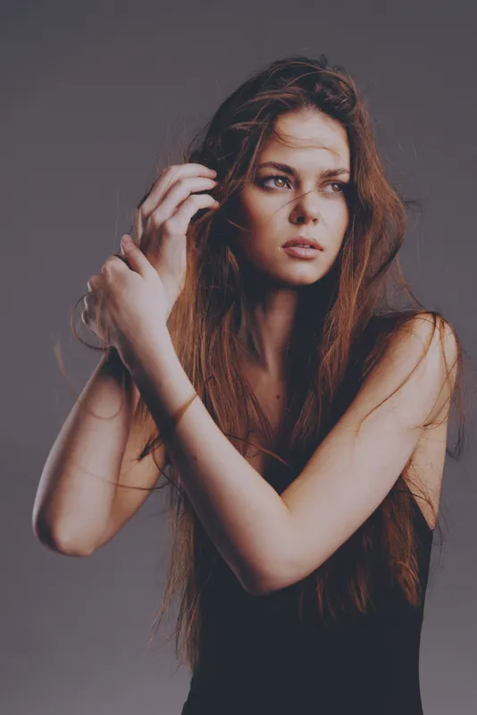 thoughtful woman with long hair in dark dress posing against gray background