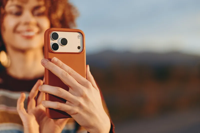 Woman lifestyle portrait outdoors, holding smartphone for a selfie, warm sunset light, soft blurred landscape background, hands and phone camera, technology communication, shallow depth of field