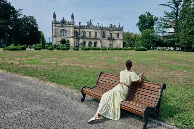 woman on bench in park facing historic estate wearing flowing dress contemplative scene with architecture and authenticity inclusivity in grounds