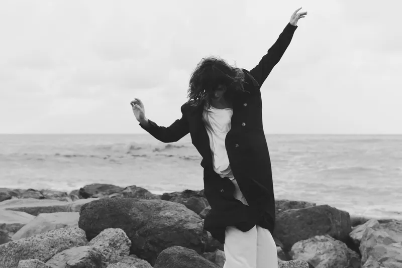 Woman on rocky shore by the seaside, outdoor scene with freedom and joy, capturing movement and candid mood in a black and white coastal moment