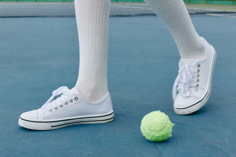 White sneakers and tennis socks on a court, with a green tennis ball, embodying an active lifestyle and sportsmanship in a sunny, outdoor setting