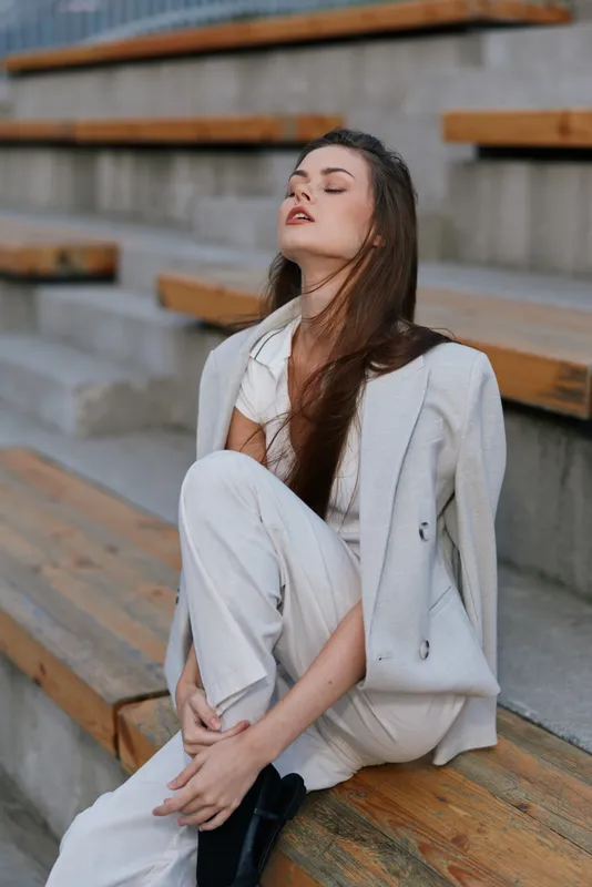 Confident businesswoman posing on wooden stairs, wearing a stylish suit and expressing a sense of calm and focus in a professional setting.