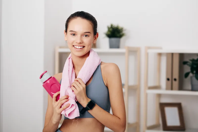 Fitness minded woman in sportswear with towel and water bottle in a bright home gym, ready for workout and training session, showing motivation and healthy lifestyle.