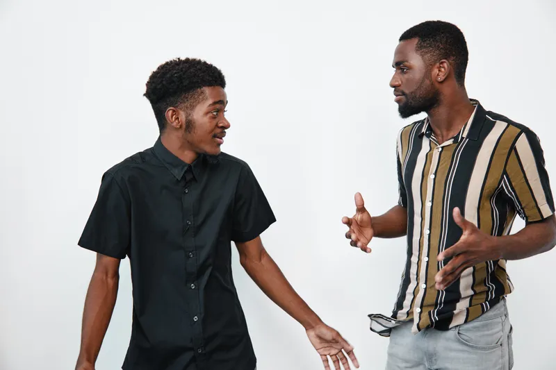 Two african american men with dark skin having a conversation and gesturing with hands in casual clothing on white background. Communication, discussion and interaction.