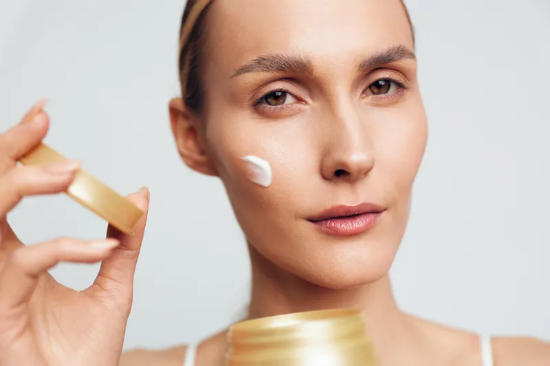 Young woman applies face serum, closeup beauty skincare routine, with cream moisturizer, smooth skin, calm expression, clean studio background.