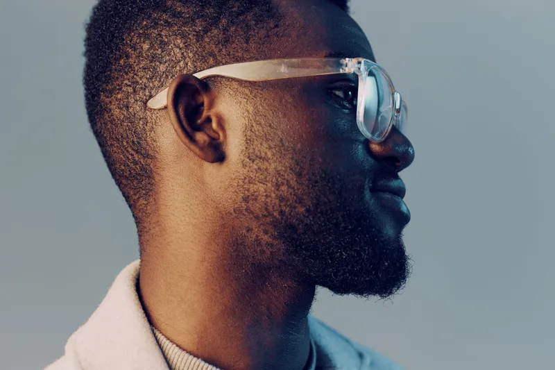 Portrait of a stylish young Black man wearing glasses, showcasing confidence and modern fashion against a soft blue background KEY portrait, stylish, Black, glasses, confidence, modern, blue, young
