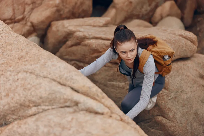 Active young woman climbing rocky terrain, showcasing determination and strength in outdoor adventure with a stylish backpack