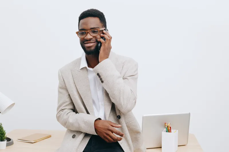 Smiling man talking on smartphone wearing smart casual suit with glasses in a bright modern office workspace. Business lifestyle concept, professional, confident, communication, technology, success, r