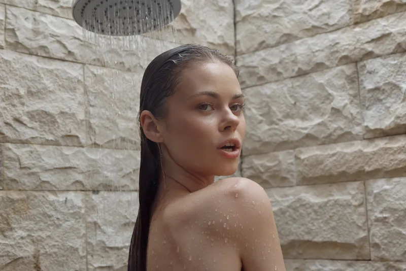 young woman taking a shower with wet hair, natural stone wall background, skin droplets, relaxed mood, indoor bathroom setting