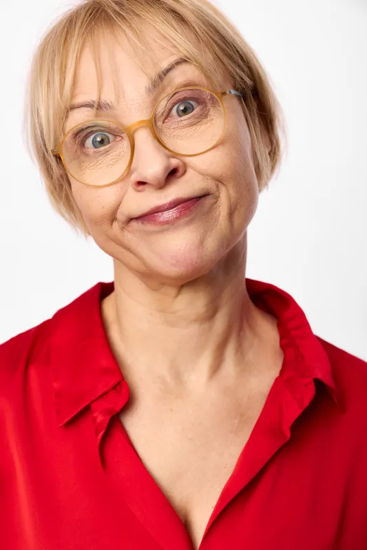 Elderly woman portrait, blonde hair, wearing glasses, gentle smile, red blouse, studio closeup on white background, calm confident expression, soft light tone