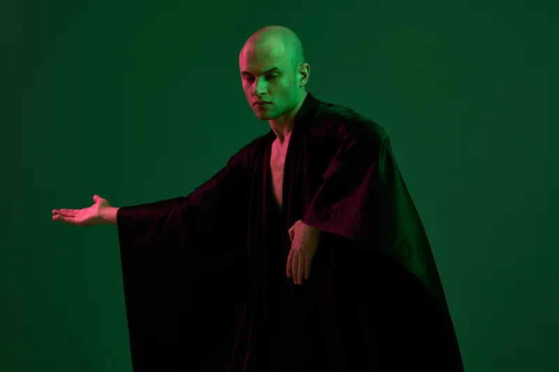 A focused man in a flowing robe strikes a confident pose against an abstract green background, showcasing an aura of mystery and intrigue in this captivating image.