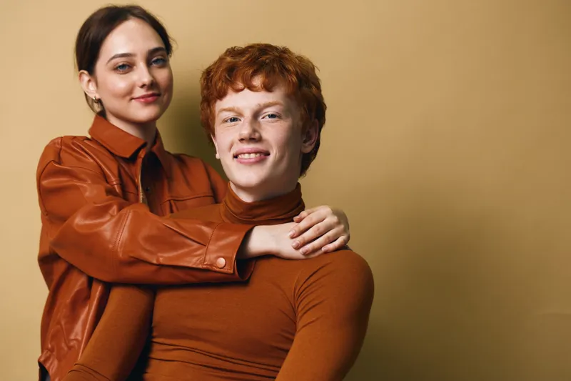 Young couple posing together with smiles and casual style against neutral background, woman hugging man with affectionate gesture for relationship and love.