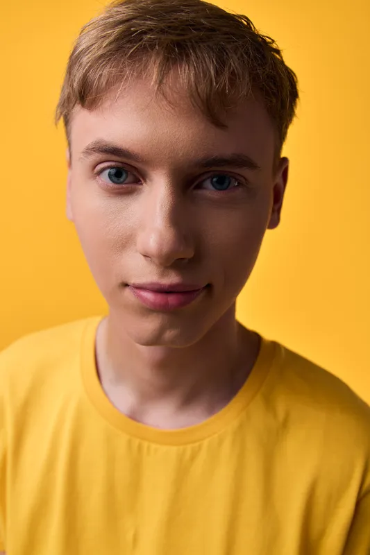 Closeup of a young boy wearing a yellow shirt against a warm yellow background, calm expression, soft studio lighting, clear eyes and smooth skin with natural details