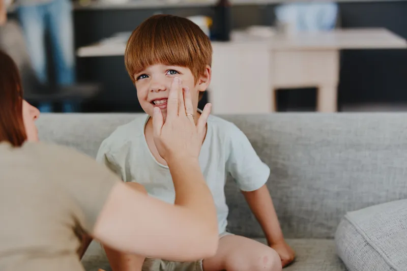 Joyful woman interacting with a smiling boy at home, creating a warm and loving atmosphere in a cozy living space filled with natural light.
