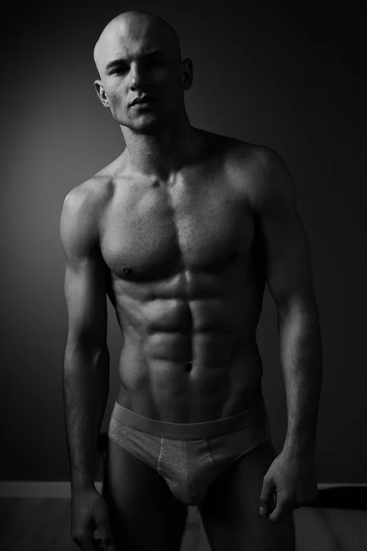 Strong man posing confidently in black and white, showcasing impressive physique and fitness, highlighting determination and strength.