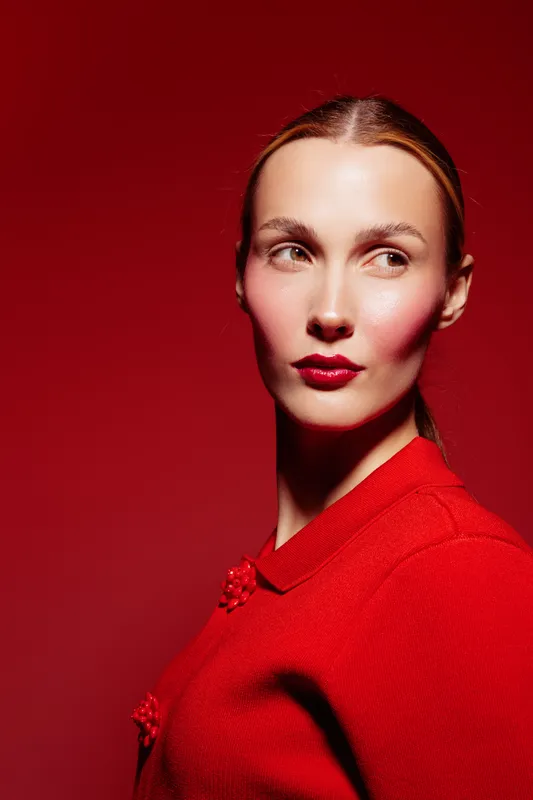 Portrait of a woman with red lipstick and red clothing looking sideways on a red background. Concept of fashion, beauty, makeup, and elegance in studio lighting.