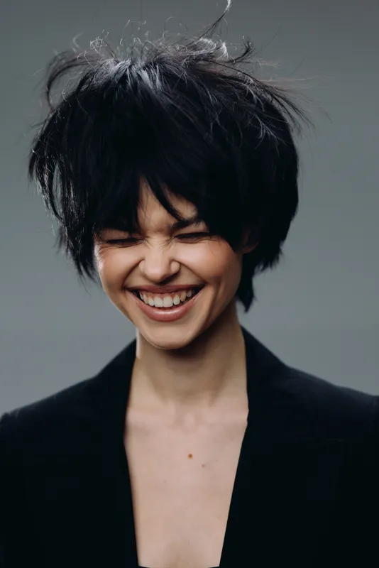 Smiling woman with short dark hair expressing joy and happiness in casual black clothing against a neutral background
