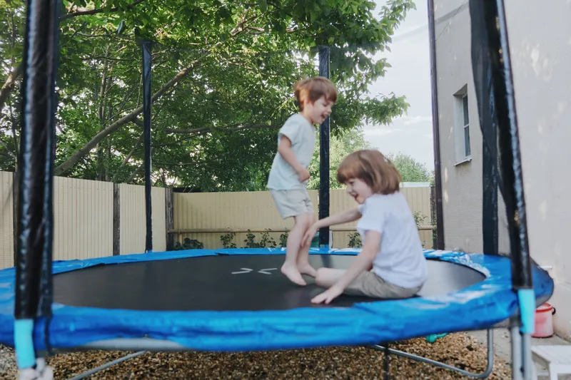 Happy children playing on a trampoline, enjoying a sunny day outdoors with greenery in the background. Perfect for family and fun-themed projects.