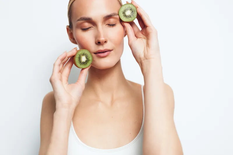 Young woman with closed eyes holds two kiwi halves near face isolated on white background natural beauty concept fresh healthy fruit skincare wellness.