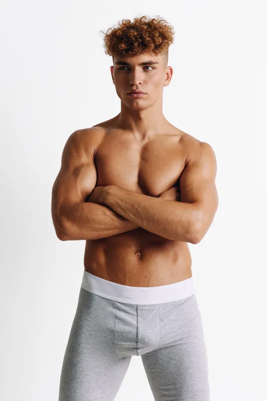 Young muscular man standing shirtless with arms crossed looking confident isolated on white background. Fitness model with athletic body showing strength and determination for healthy lifestyle goals.