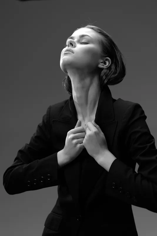 Black and white portrait of a confident woman in a blazer with closed eyes, expressing strength and elegance in a minimalist studio setting.