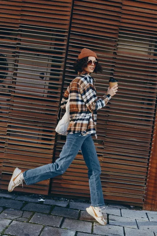 Woman with coffee walking in urban autumn streets, candid and stylish portrait capturing authenticity and mindful living with golden hour glow, emotional storytelling in city lifestyle.