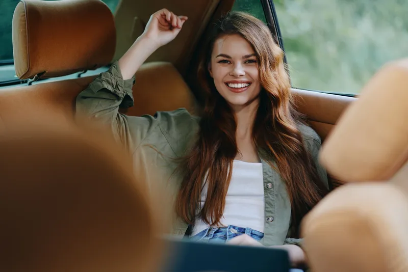 Young woman smiling in a car, wearing casual attire with a relaxed vibe, showcasing warmth and happiness in a cozy, natural setting.