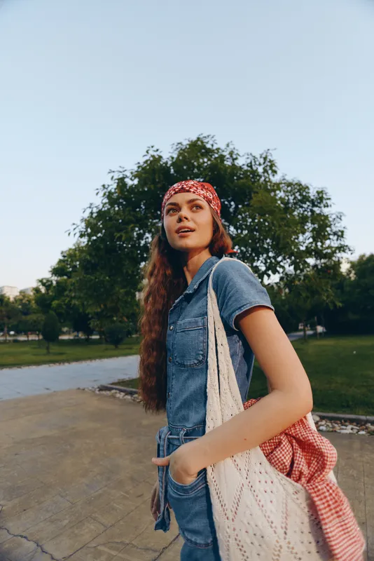 Modern boho-western denim street style woman with long hair and red bandana walking outdoors in lifestyle setting, film color tones enhancing natural summer atmosphere.