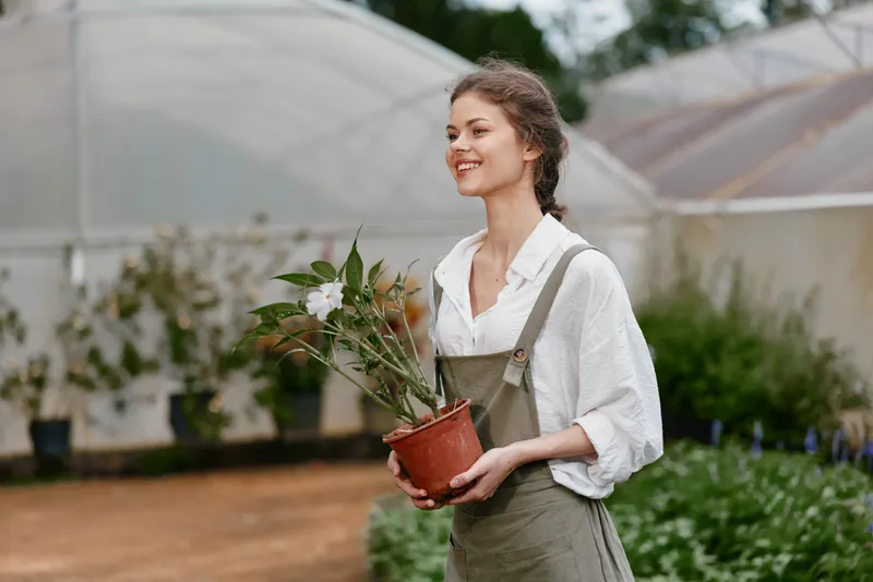 Young woman in greenhouses holding potted plant, showcasing gardening, joy, and sustainability Perfect for eco friendly themes and seasonal gardening concepts