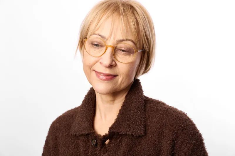 Woman elderly glasses portrait, smiling in closeup, wearing warm coat and teddy collar, calm senior female headshot with eyewear on white studio soft light indoor background.